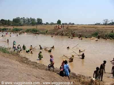People fishing with nets in a muddy river, women in saris on the bank