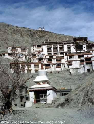 white Buddhist monastery perched on the mountain, whitewashed stupa in front, blue sky