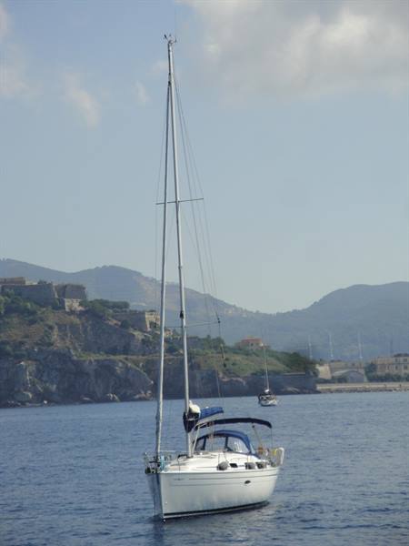 White sailboat at anchor, hills and old fortifications in the background