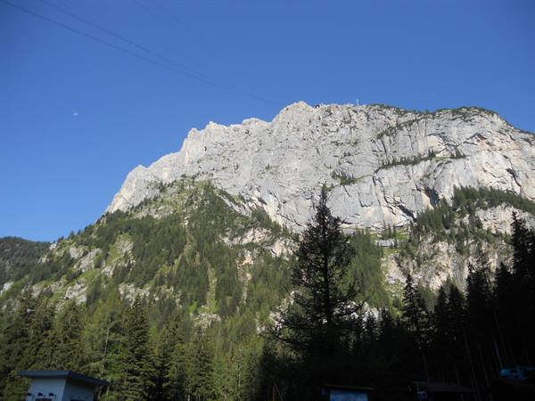 Limestone cliff above conifer forest, cable car line and blue sky