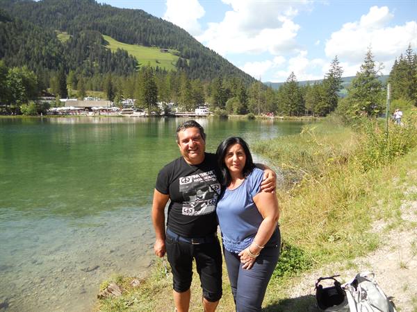 Couple smiling on grassy shore of a green alpine lake among firs