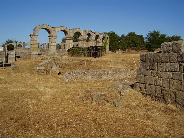 Ancient Roman stone aqueduct arches among dry grass at Vulci
