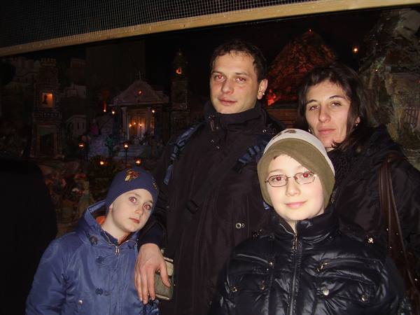 Family posing before an illuminated nativity scene with figurines and lights