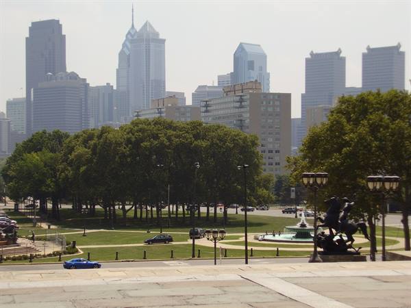 Philadelphia skyscrapers above green park with fountain and horse statues