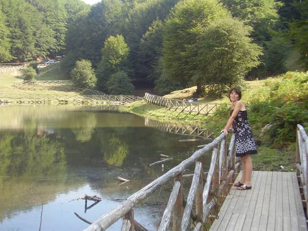 Woman in polka dot dress on wooden boardwalk beside a small forest lake