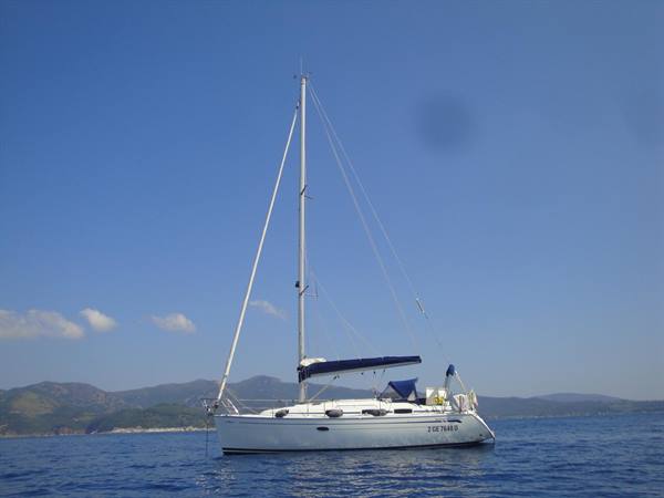 White sailboat anchored on blue sea, green mountains in the background