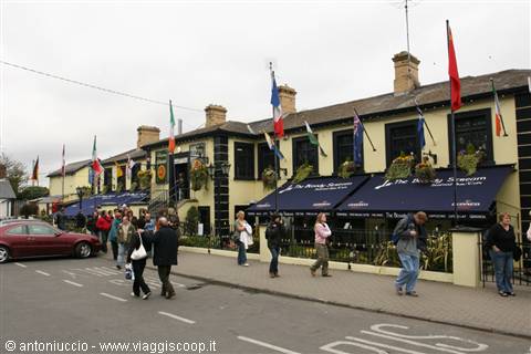Tourists walking past a pub with international flags and blue awnings
