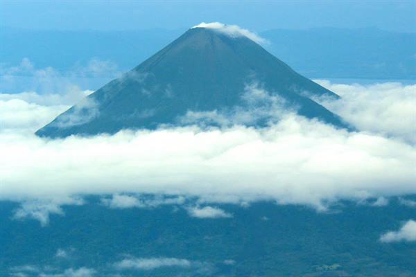 Conical volcano with snowy peak emerging above white clouds