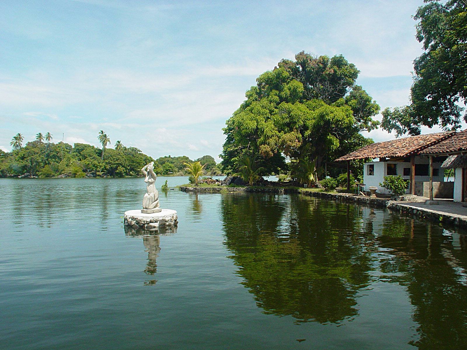 White statue on tiny islet, tiled-roof house and lush trees by the lake