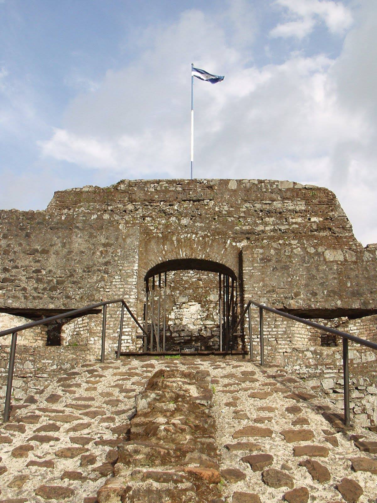 Honduras flag flying over an old stone fort with an arched gateway