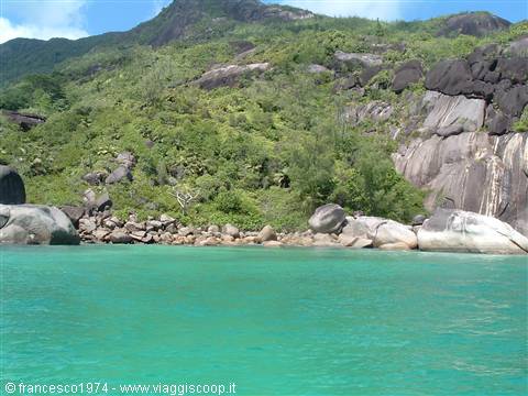 Turquoise water in front of giant granite boulders and green hill, Seychelles
