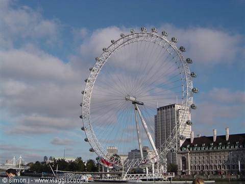 The steel London Eye rises over the Thames among clouds and buildings