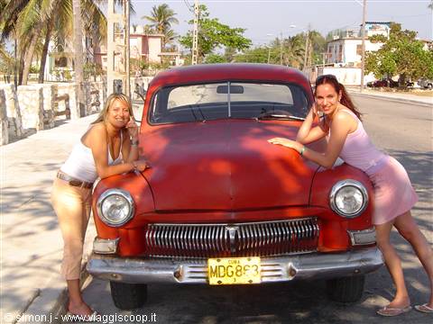 Two women leaning on a vintage red car on a sunny street