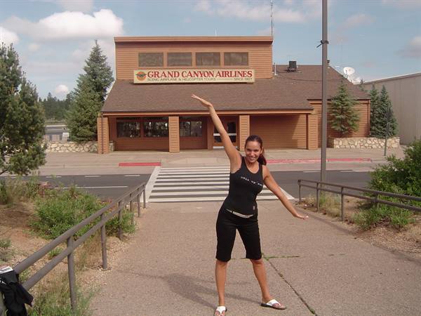 Woman in black poses with raised arm in front of Grand Canyon Airlines, Tusayan