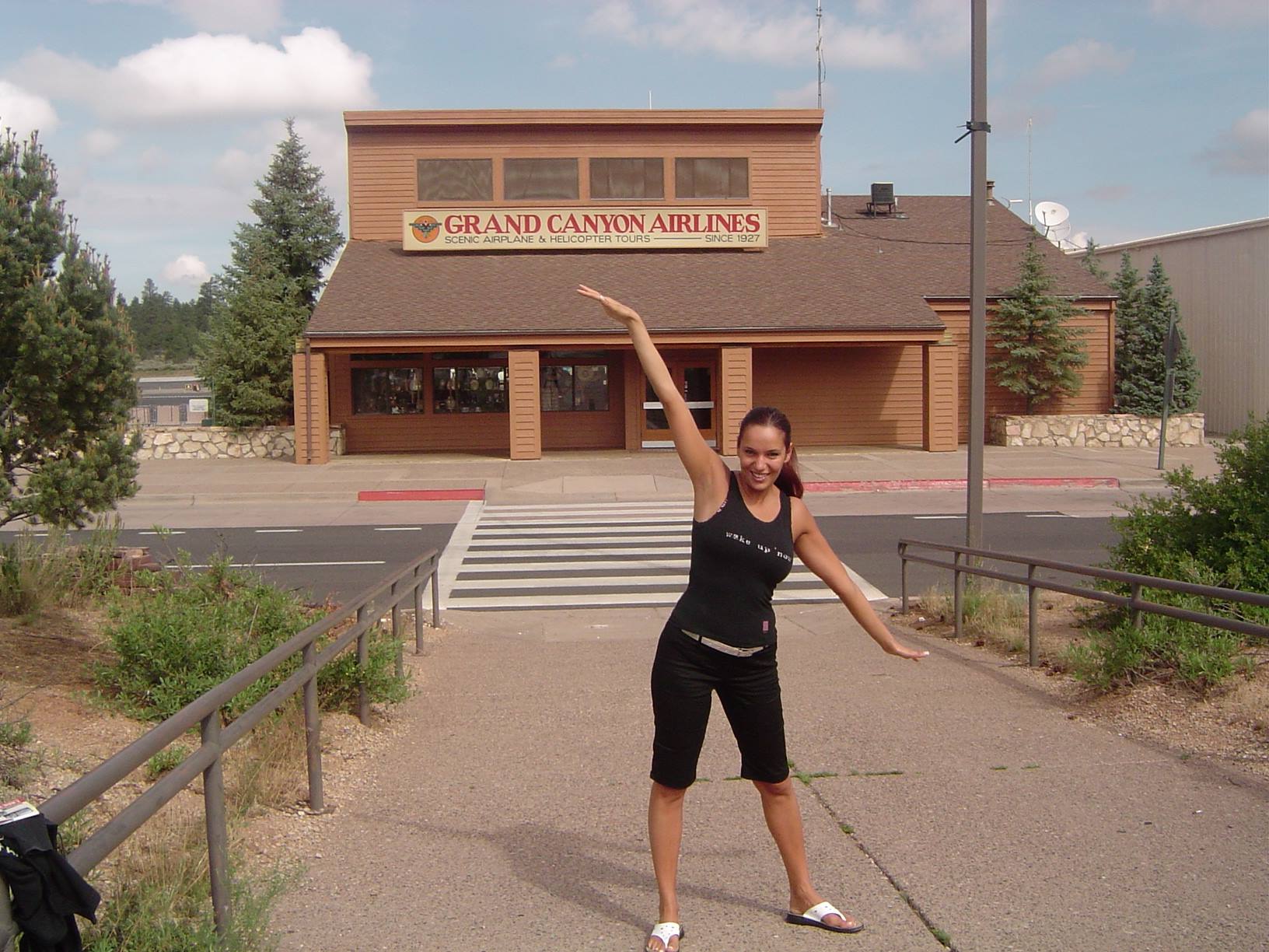 Woman in black poses with raised arm in front of Grand Canyon Airlines, Tusayan