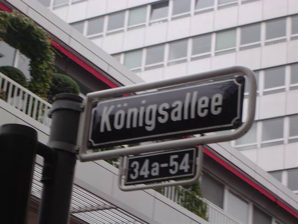 Black Königsallee street sign in front of a grid-facade building