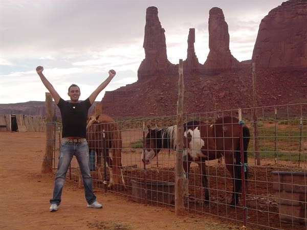Tourist raising arms next to fenced horses, Monument Valley