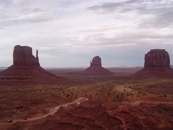 Monument Valley, red sandstone buttes rising over sandy desert under cloudy sky