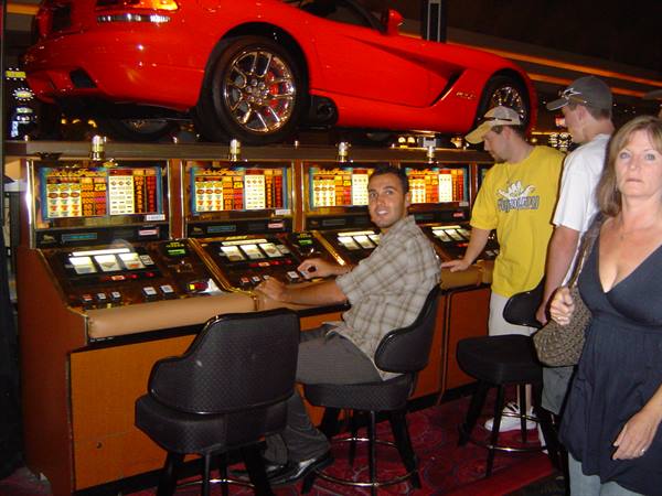 Man playing slot machines beneath a red Dodge Viper, Las Vegas casino