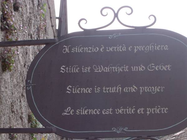 Oval iron sign with multilingual writing about silence, hanging on a stone wall