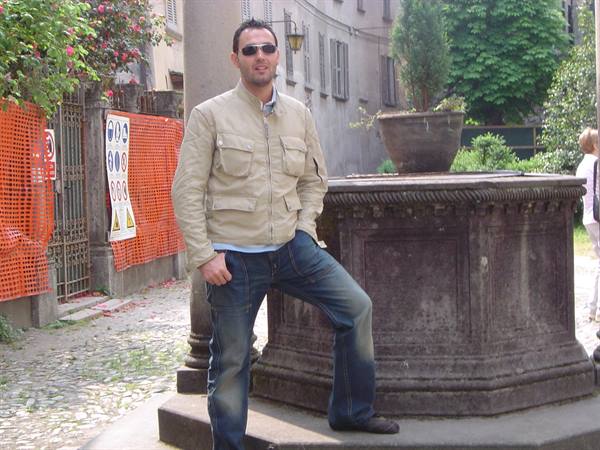 Man in beige jacket and sunglasses leaning on an old stone fountain on cobblestones
