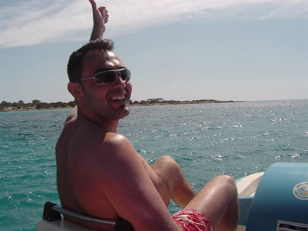 Man in sunglasses on blue dinghy giving thumbs up, turquoise sea