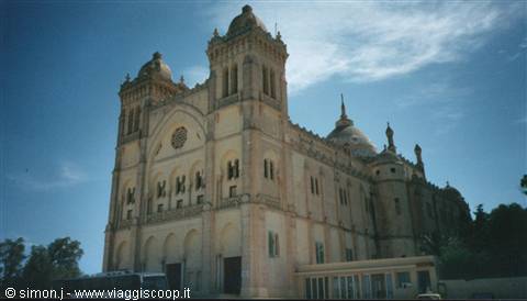 Light stone cathedral with twin towers and dome under blue sky