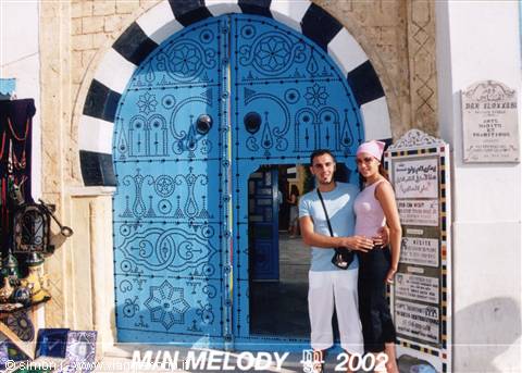 Couple posing before an ornate blue door with black-and-white arch