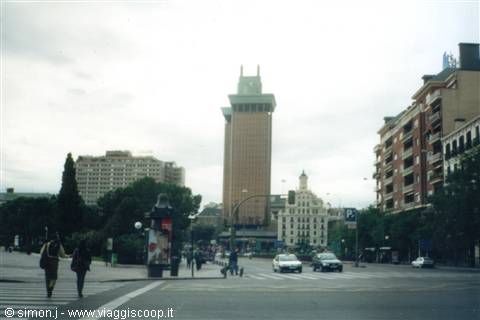 Pedestrians and cars cross the square by Torres de Colón, overcast sky