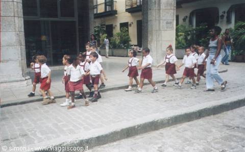 Schoolchildren in red and white uniforms walk in line with their teacher