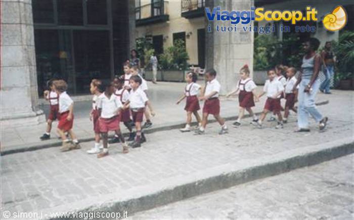 Schoolchildren in red and white uniforms walk in line with their teacher