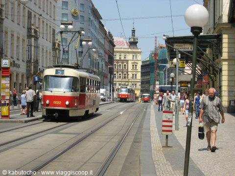 Red and cream trams run along tracks on a busy Prague street