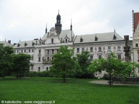 Historic palace with grey roof and spires, green lawn and trees in front