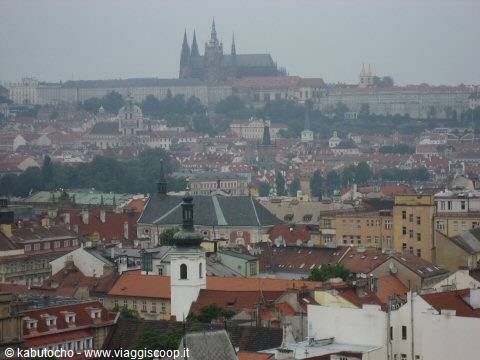 Prague Castle and gothic spires rising above red rooftops in mist