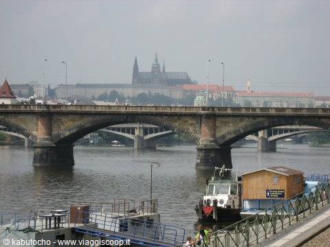 Stone bridge over the Vltava, a moored boat below, Prague Castle in the haze