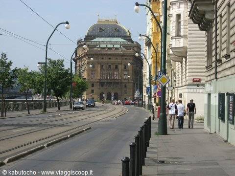 Pedestrians walk along the sidewalk by the Prague National Theatre