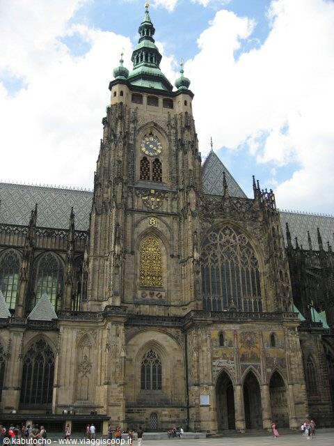 Gothic dark stone towers of St. Vitus Cathedral, golden clock, tourists below