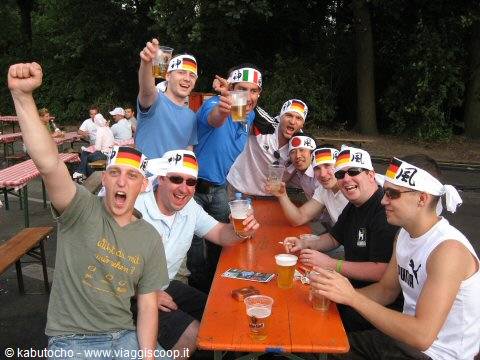 Fans in German and Japanese headbands toast with beers at beer garden tables