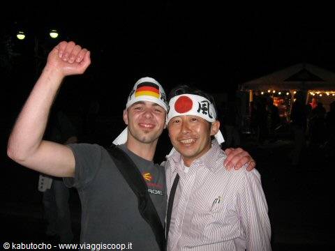 Two smiling men wearing German and Japanese headbands at night