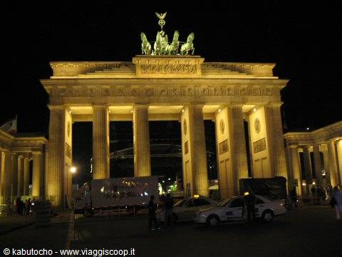 Brandenburg Gate lit up at night, cars and people by the columns