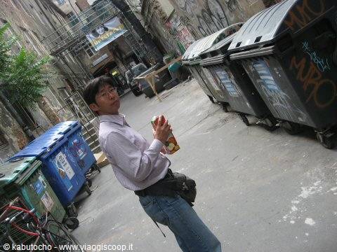 Man holding bottle next to dumpsters, alley with graffiti and scaffolding
