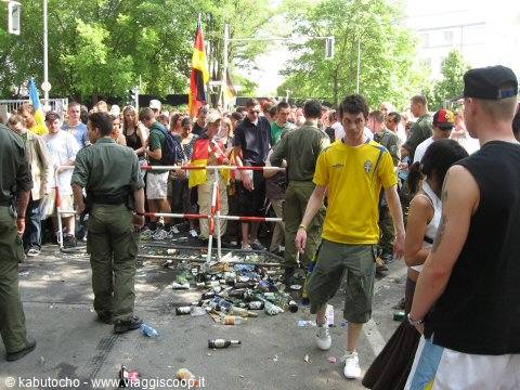 Crowd with German flags and police behind barriers, bottles scattered on the ground