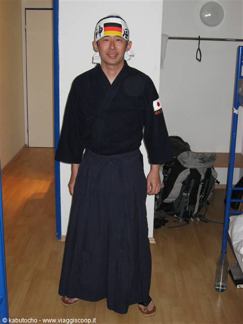 Man in black kimono and hakama wearing German headband, in a hostel