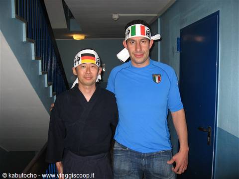 Two men wearing Japanese and Italian headbands indoors, blue staircase