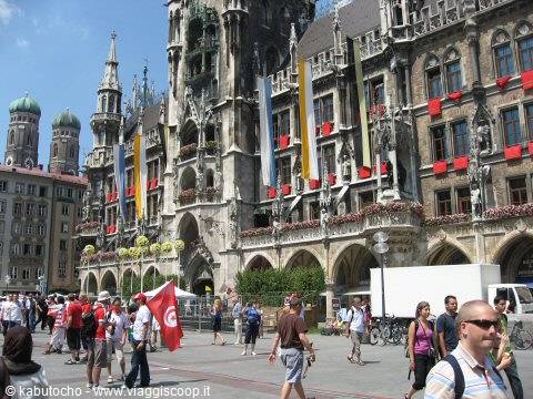 Tourists walking past Munich's Gothic Neue Rathaus, flags and flower decorations