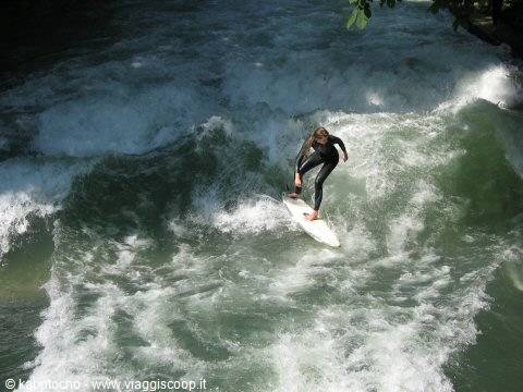Surfer in black wetsuit rides the Eisbach river wave in Munich
