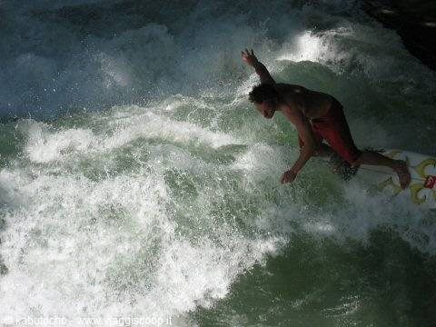 Surfer in red shorts riding the Eisbach river wave in Munich