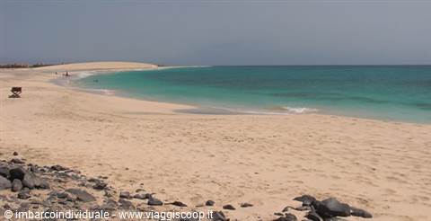 White sand beach with black rocks, turquoise water and distant dune, Corralejo