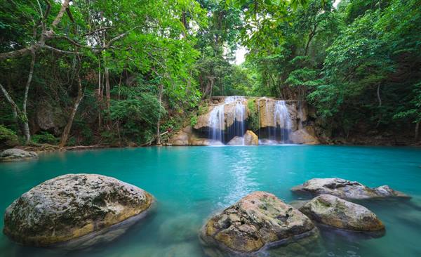 Waterfall among green trees plunges into turquoise pool with limestone rocks