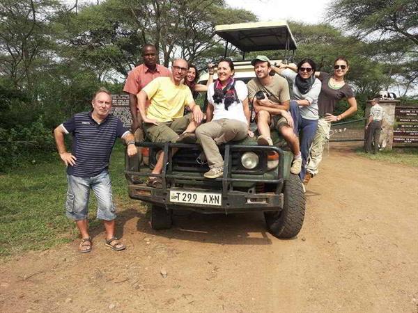 Group of tourists posing on a green safari jeep at a park entrance gate